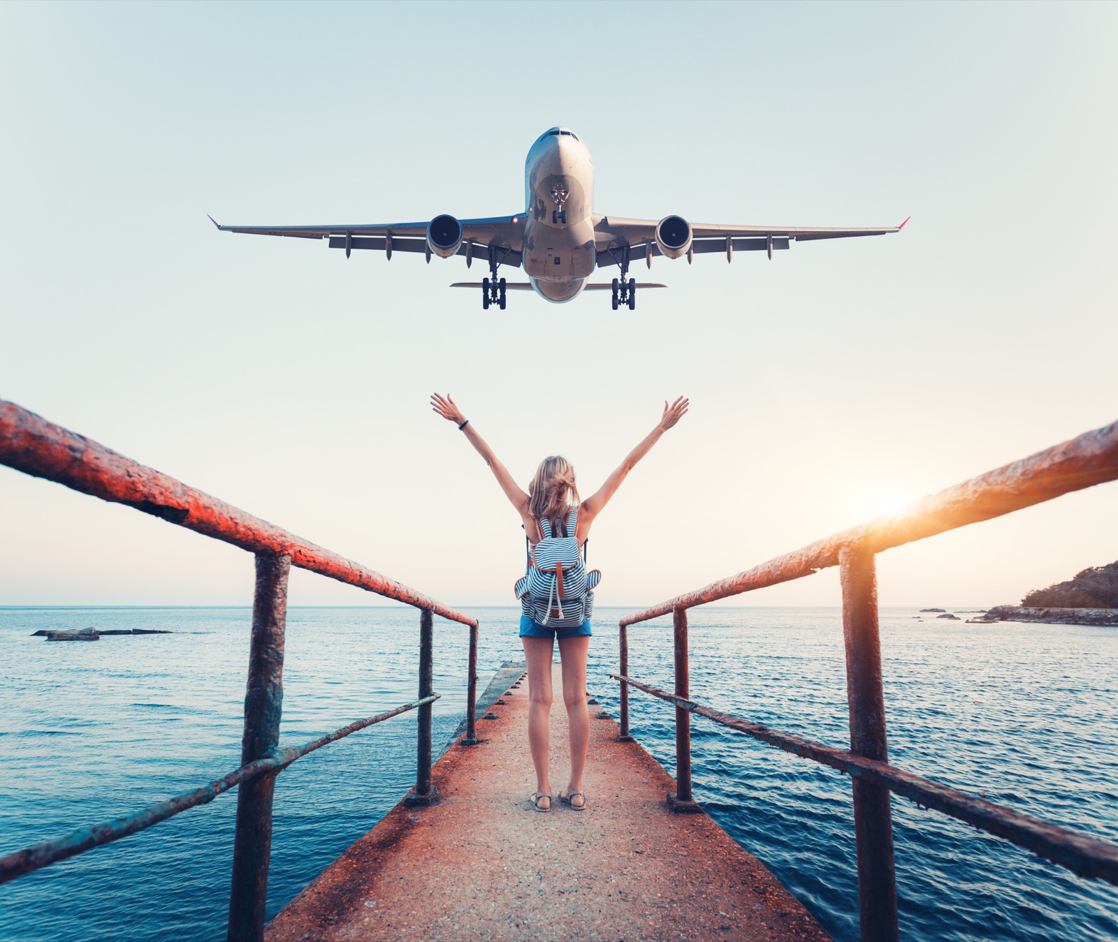 ✈️ Travel Somewhere for Each Letter of the Alphabet and We’ll Tell You Your Fortune Airplane And Woman At Sunset. Summer Landscape With Girl Standing On The Sea Pier With Raised Up Arms And Flying Passenger Airplane. Woman And Landing Commercial Plane In The Evening. Lifestyle