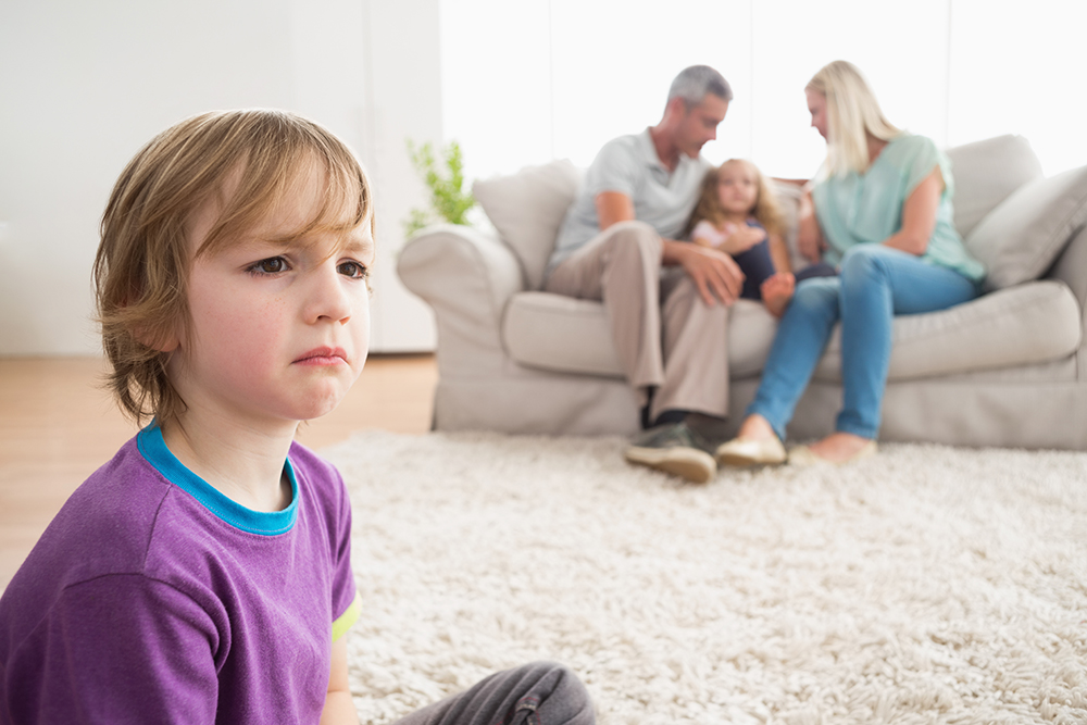 Memory Test Upset boy sitting on floor while parents enjoying with sister on sofa at home