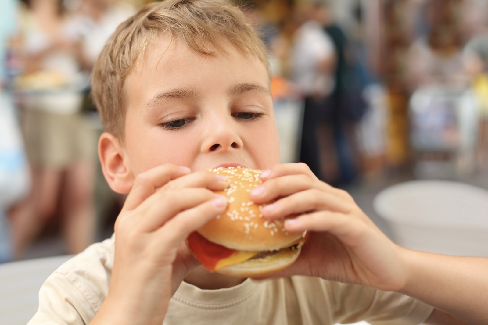 ABC General Knowledge Trivia little caucasian boy eating burger, looking down