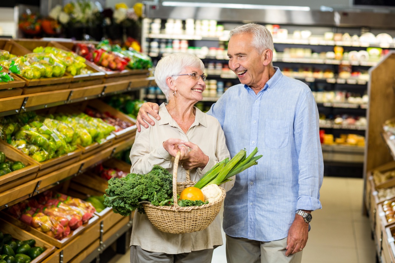 Smiling,Senior,Couple,Holding,Basket,With,Vegetables,At,The,Grocery